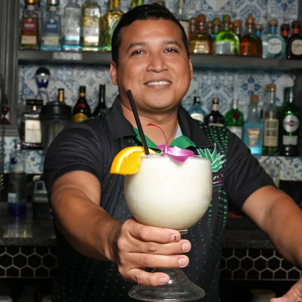 Smiling bartender at El Mezcal Mexican Restaurant holding out a frozen margarita with an orange slice.