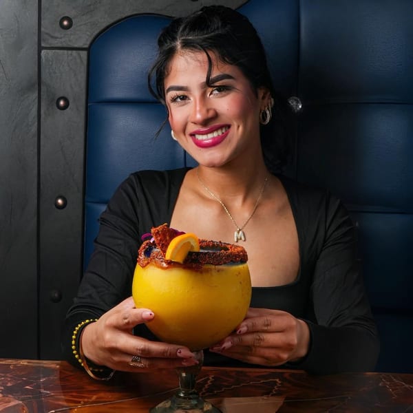 Smiling woman holding a large yellow El Mezcal Mexican Restaurant drink with a chili-lime rim.